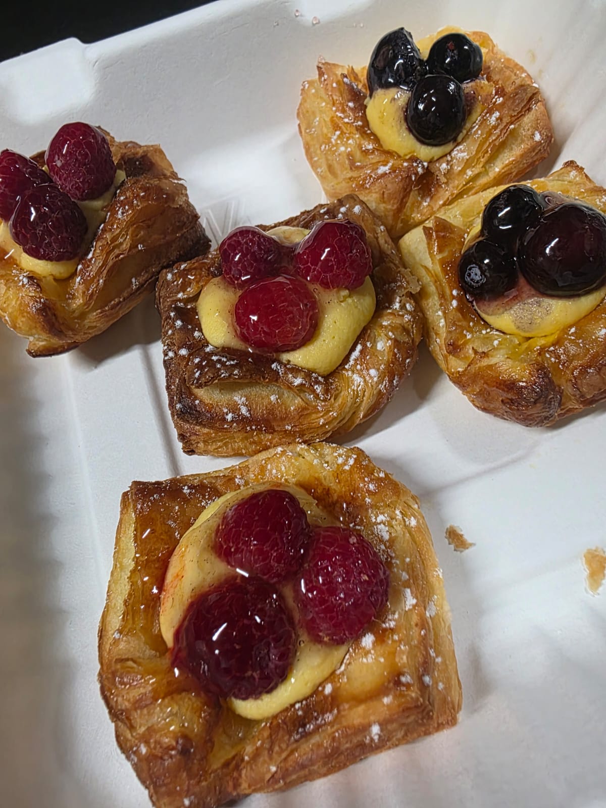 Four small raspberry and blueberry danishes packed into a takeaway box